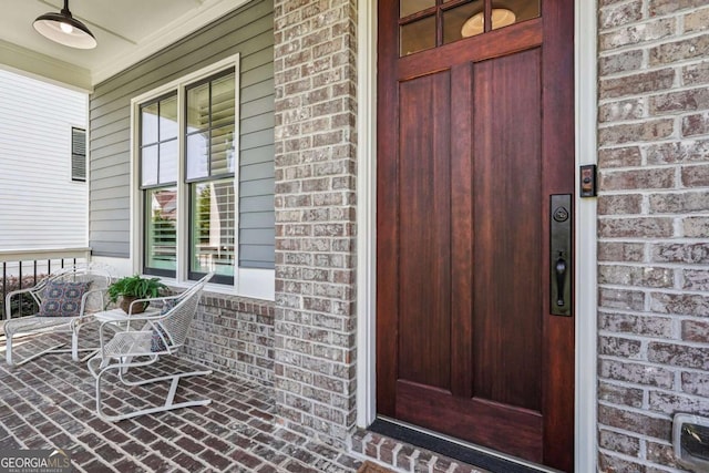 property entrance featuring a porch, brick siding, and ceiling fan