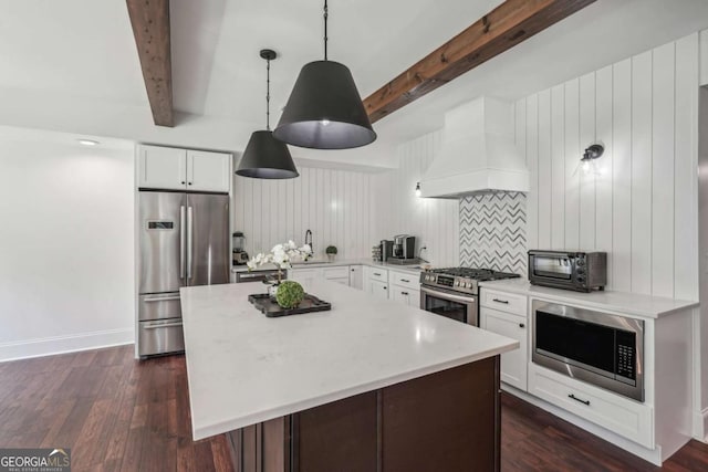 kitchen with a toaster, a kitchen island, appliances with stainless steel finishes, premium range hood, and beam ceiling