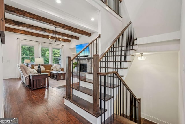 staircase with hardwood / wood-style flooring, a notable chandelier, baseboards, and beamed ceiling