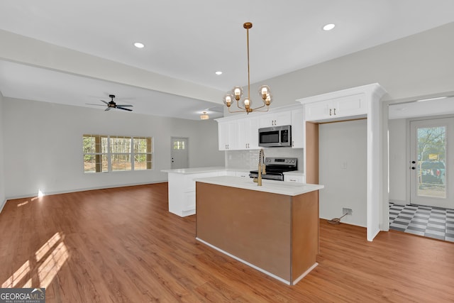 kitchen with an island with sink, light wood-style flooring, stainless steel appliances, light countertops, and white cabinetry