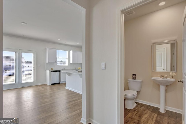 half bathroom with baseboards, toilet, backsplash, wood finished floors, and a sink