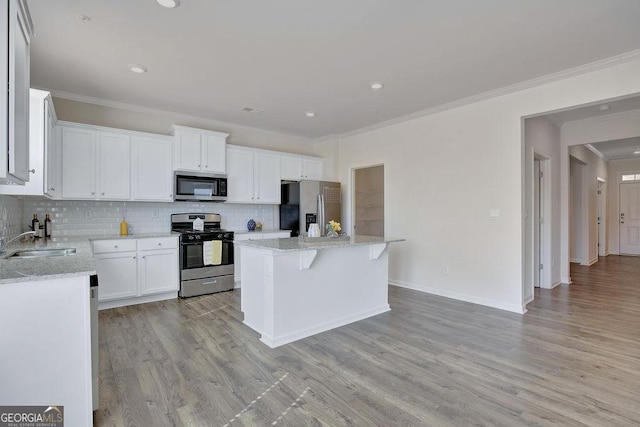 kitchen featuring a kitchen island, a sink, appliances with stainless steel finishes, light wood finished floors, and tasteful backsplash