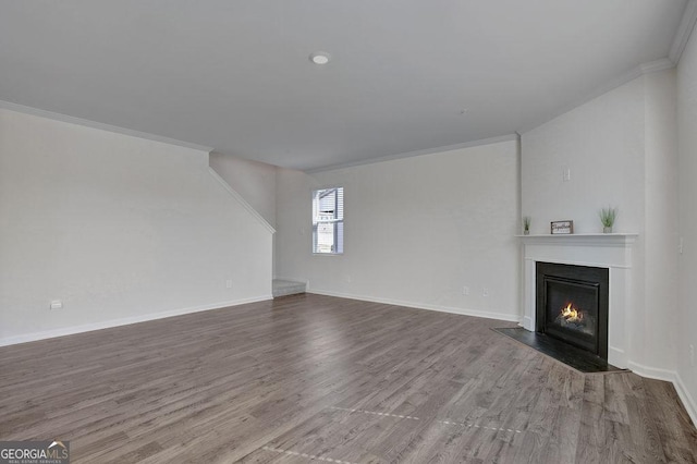 unfurnished living room with baseboards, wood finished floors, a fireplace with flush hearth, and crown molding