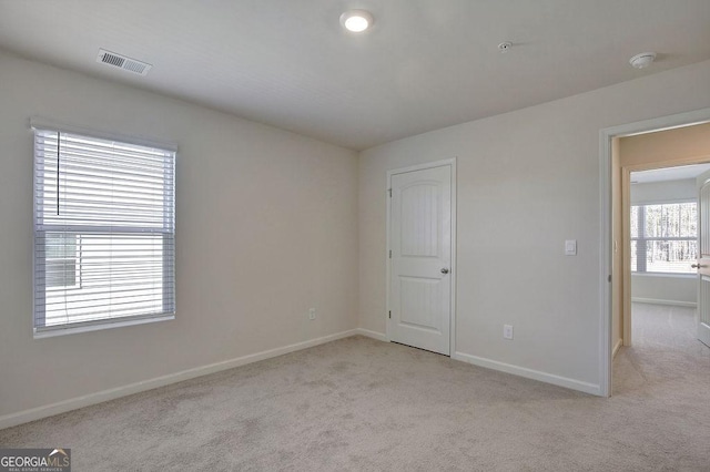 spare room featuring light colored carpet, visible vents, and baseboards