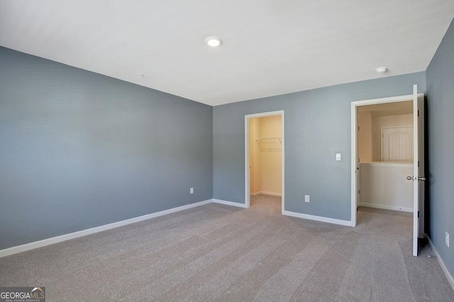 unfurnished bedroom with a closet, baseboards, a walk in closet, and carpet flooring