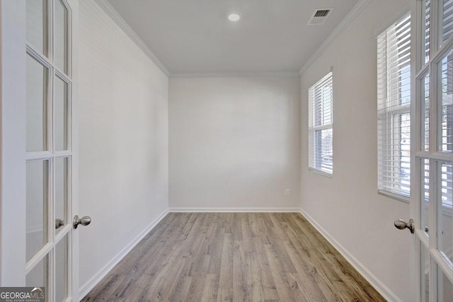 spare room with baseboards, light wood-style floors, visible vents, and crown molding