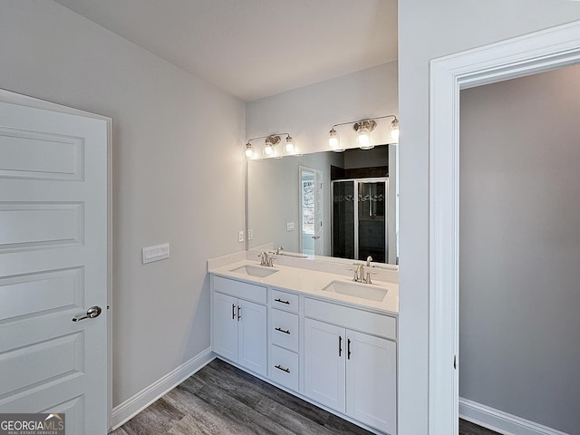 full bathroom featuring baseboards, double vanity, a sink, and a shower stall