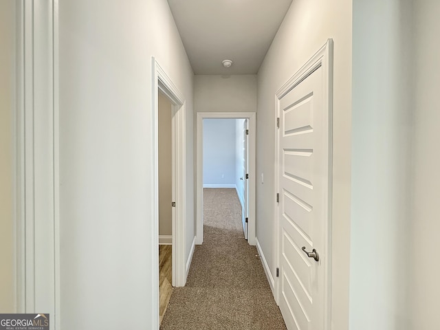 hallway with baseboards and dark colored carpet