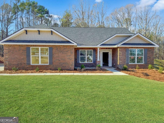 craftsman inspired home featuring a shingled roof, a front yard, and brick siding