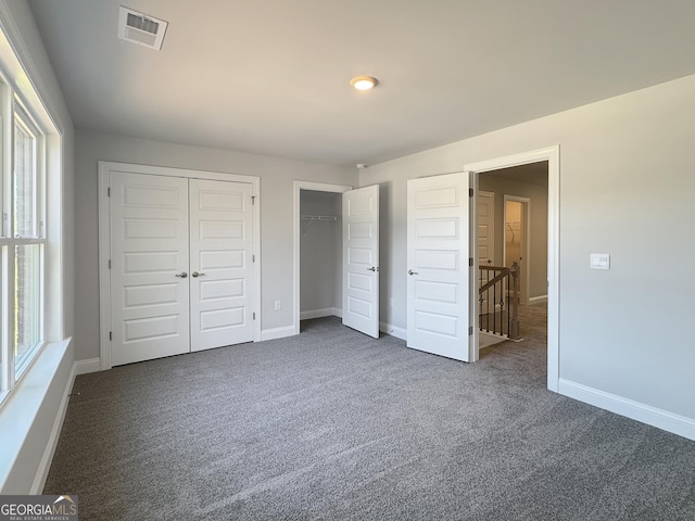 unfurnished bedroom featuring visible vents, dark carpet, baseboards, and two closets