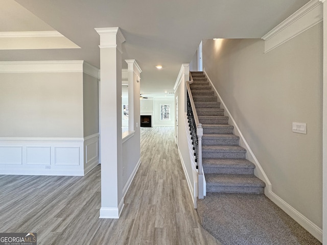 staircase with a decorative wall, a fireplace, wood finished floors, and crown molding