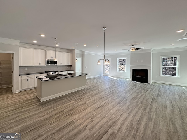 kitchen featuring dark countertops, appliances with stainless steel finishes, open floor plan, crown molding, and white cabinetry