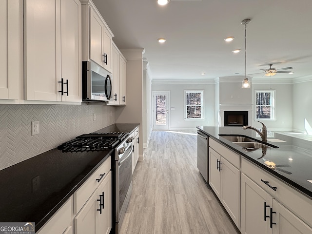 kitchen with a fireplace, a sink, open floor plan, appliances with stainless steel finishes, and ornamental molding