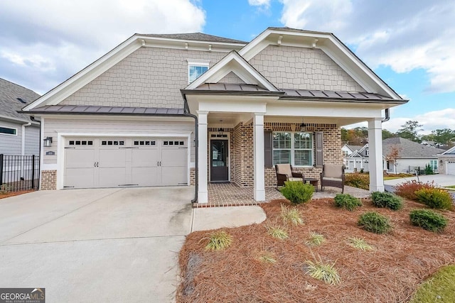 craftsman inspired home featuring a garage, concrete driveway, a standing seam roof, a porch, and brick siding