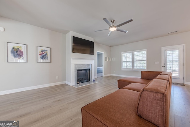 living area with visible vents, light wood-style flooring, a premium fireplace, a ceiling fan, and baseboards