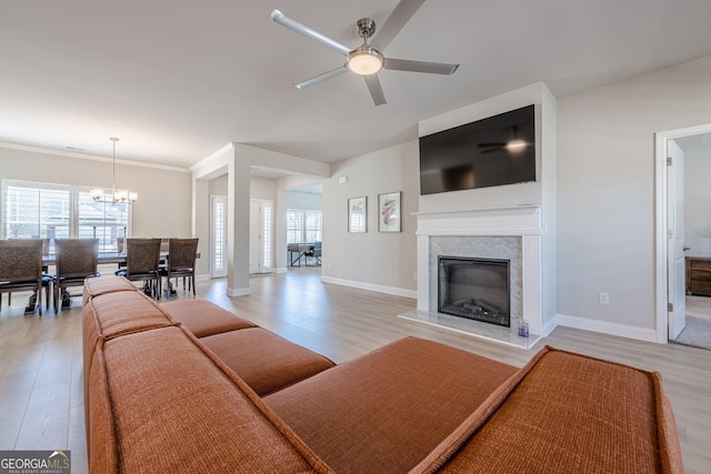 living area with light wood finished floors, a premium fireplace, baseboards, and ceiling fan with notable chandelier