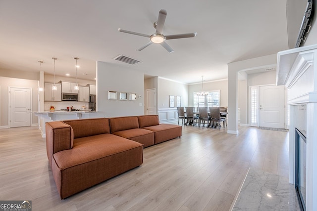 living room with light wood-style floors, visible vents, ornamental molding, and ceiling fan with notable chandelier