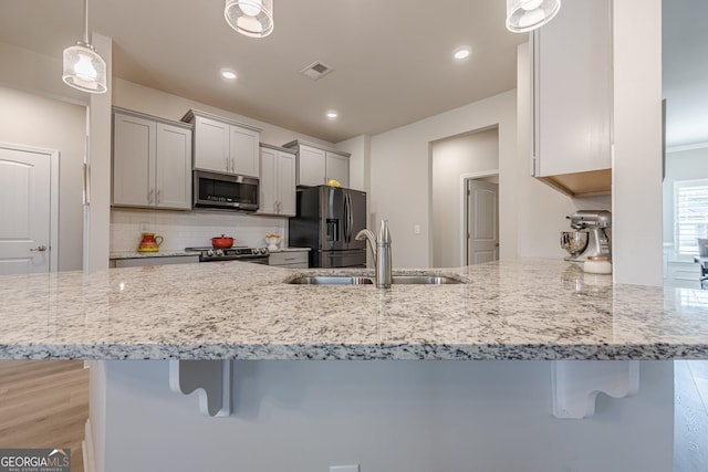 kitchen with stainless steel appliances, gray cabinets, a sink, and a breakfast bar area