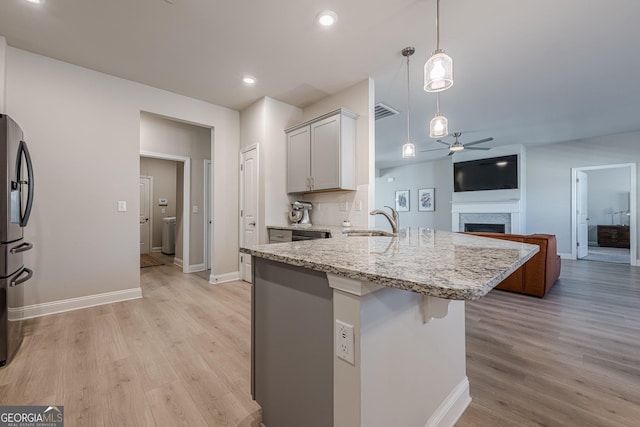 kitchen featuring ceiling fan, a fireplace, a sink, light wood-type flooring, and stainless steel fridge with ice dispenser