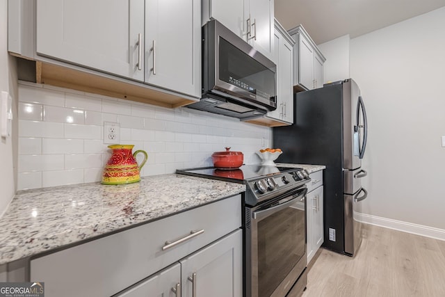 kitchen with baseboards, light stone countertops, stainless steel appliances, light wood-style floors, and backsplash