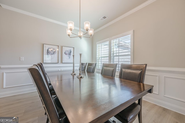 dining area with a decorative wall, visible vents, light wood-style floors, ornamental molding, and wainscoting