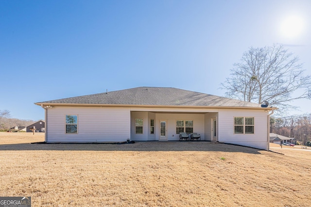 rear view of property featuring a yard, a shingled roof, and a patio area