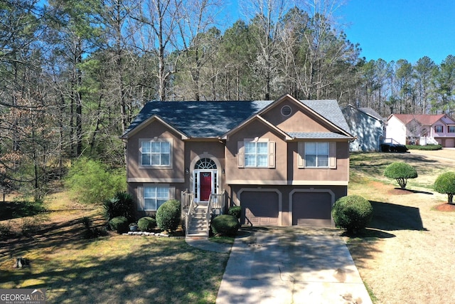 raised ranch with an attached garage, a front yard, concrete driveway, and stucco siding