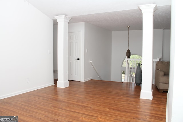 interior space with decorative columns, a textured ceiling, baseboards, and wood finished floors