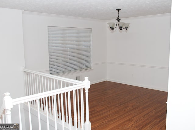 spare room featuring a notable chandelier, visible vents, ornamental molding, a textured ceiling, and wood finished floors