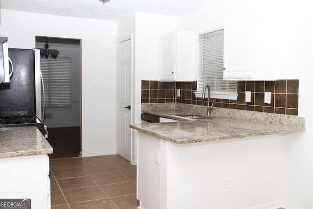 kitchen featuring a peninsula, a sink, white cabinets, freestanding refrigerator, and decorative backsplash