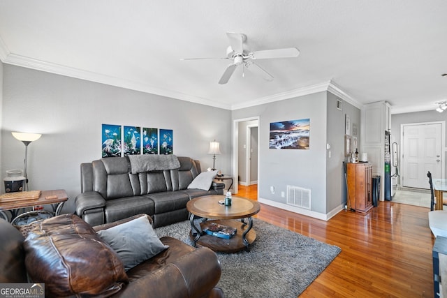 living room with ceiling fan, wood finished floors, visible vents, baseboards, and ornamental molding