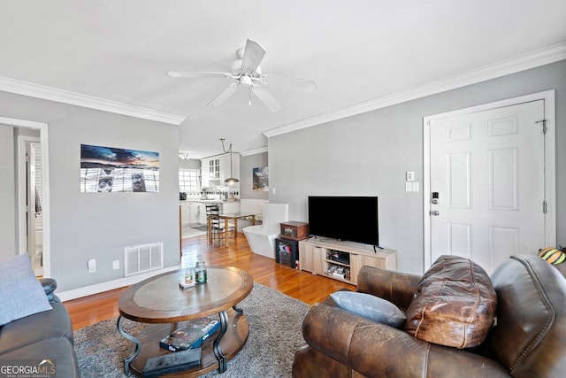 living area featuring crown molding, visible vents, a ceiling fan, wood finished floors, and baseboards