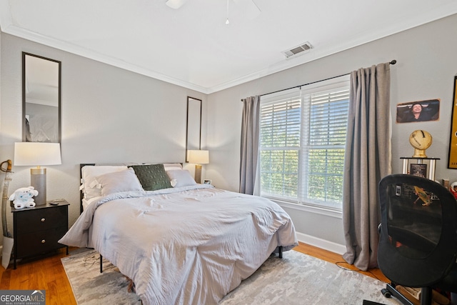 bedroom with baseboards, crown molding, visible vents, and wood finished floors