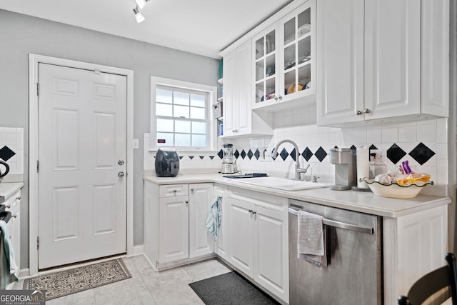 kitchen featuring tasteful backsplash, white cabinets, dishwasher, glass insert cabinets, and a sink