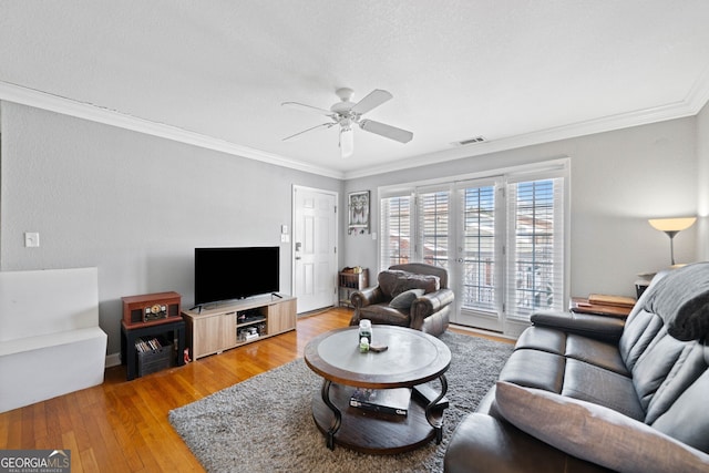 living area with ceiling fan, light wood finished floors, visible vents, and crown molding