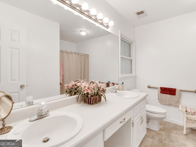 full bath featuring toilet, double vanity, visible vents, and a sink