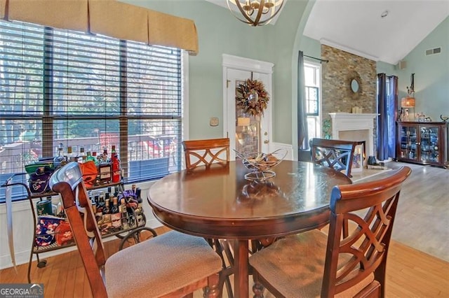 dining room with arched walkways, a fireplace, visible vents, vaulted ceiling, and wood finished floors