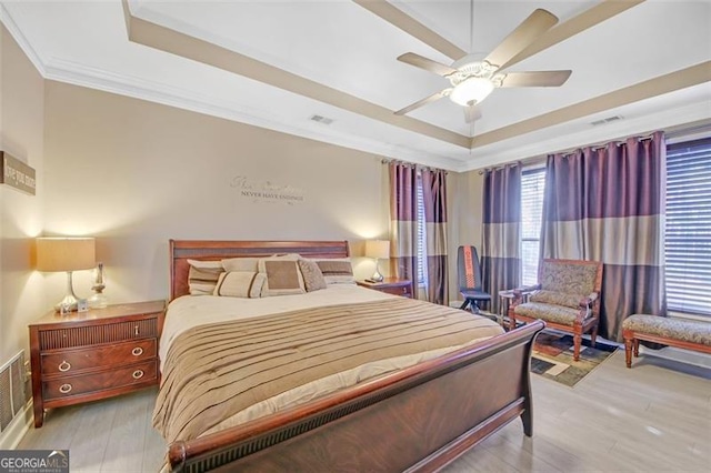 bedroom featuring visible vents, a tray ceiling, crown molding, and wood finished floors