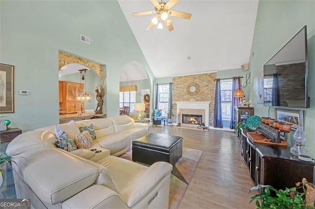 living room featuring light wood finished floors, visible vents, a ceiling fan, high vaulted ceiling, and a lit fireplace