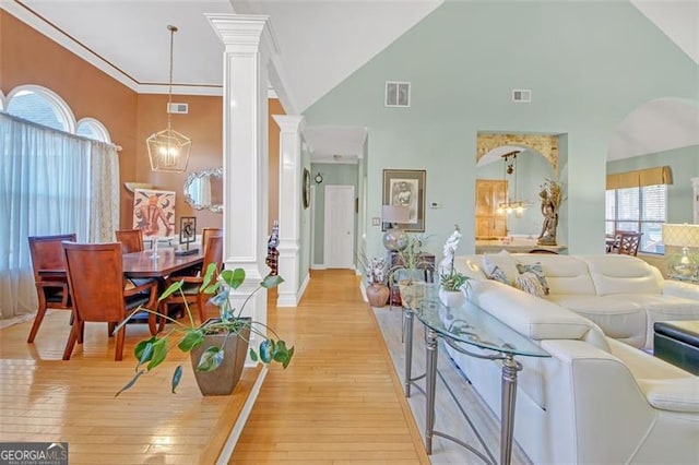 living room featuring ornate columns, visible vents, a chandelier, and light wood finished floors