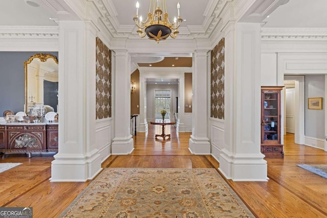 interior space featuring an inviting chandelier, decorative columns, a decorative wall, and crown molding