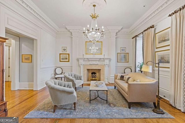 living area featuring crown molding, a decorative wall, an inviting chandelier, a high end fireplace, and wood finished floors