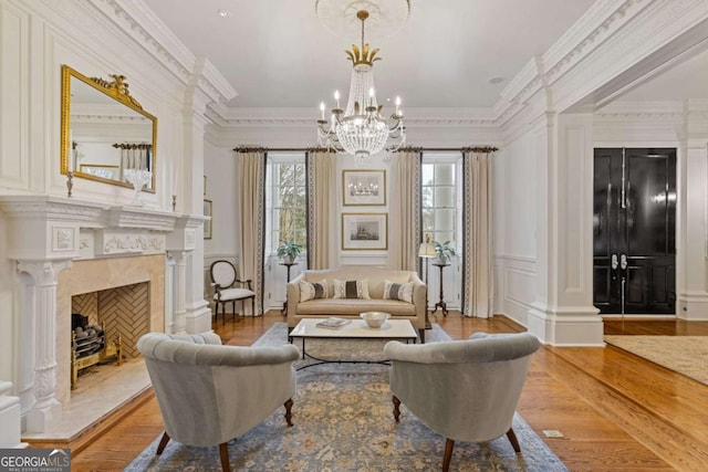 sitting room featuring ornamental molding, decorative columns, a premium fireplace, and wood finished floors