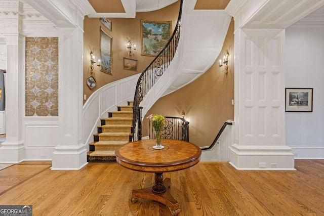 stairway with decorative columns, a wainscoted wall, wood finished floors, crown molding, and a decorative wall