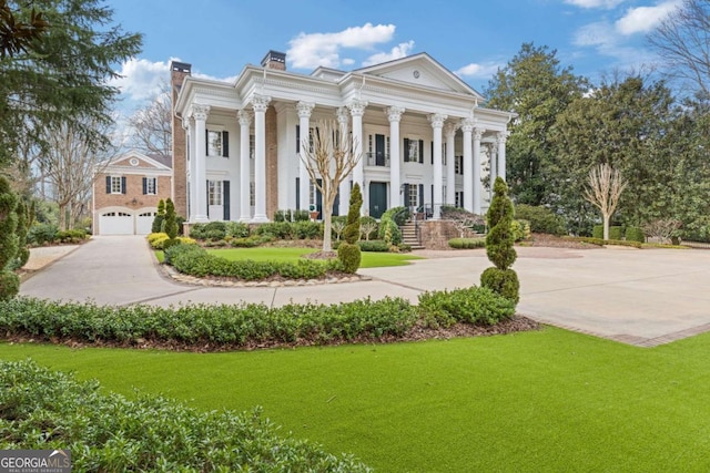 greek revival inspired property with a front yard, driveway, and a chimney