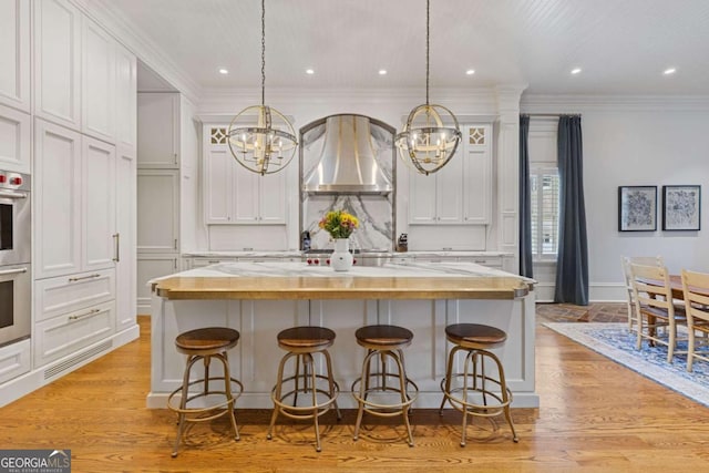 kitchen with ornamental molding, decorative backsplash, light wood finished floors, and wall chimney exhaust hood