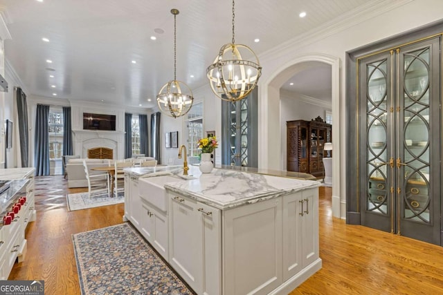 kitchen featuring arched walkways, white cabinets, open floor plan, light wood-style floors, and a sink