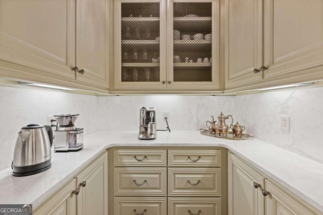 kitchen with glass insert cabinets, cream cabinetry, light countertops, and decorative backsplash