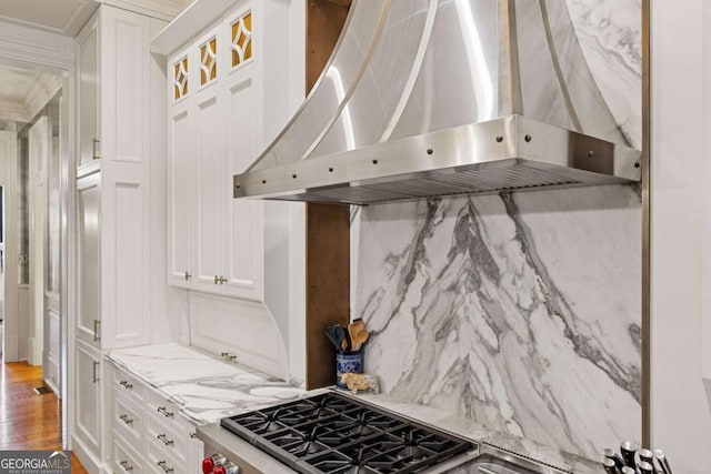 kitchen featuring white cabinetry, wall chimney range hood, light stone countertops, tasteful backsplash, and glass insert cabinets