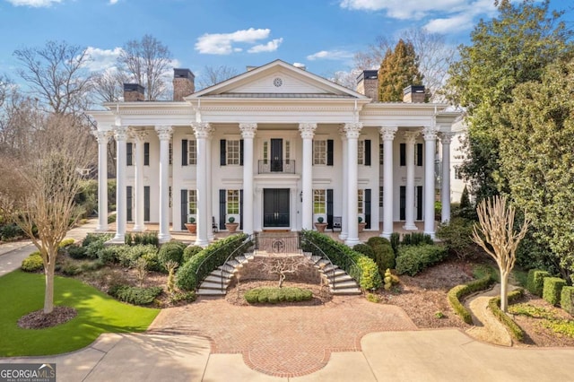 neoclassical home featuring covered porch, stairs, and a chimney